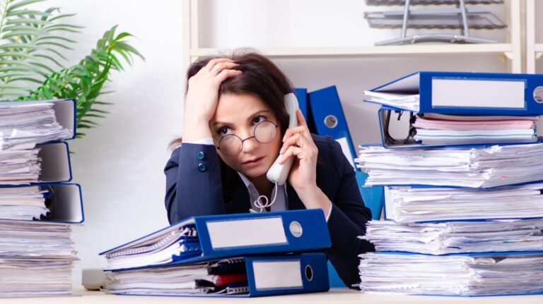 woman littered with folders with works speaks on the phone