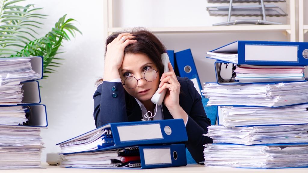 woman littered with folders with works speaks on the phone